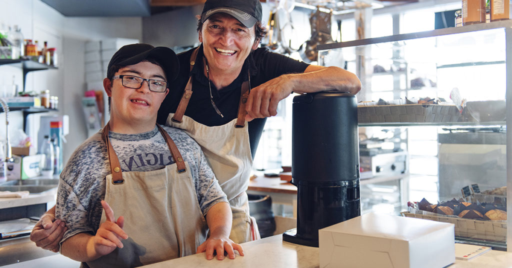 A boy with Down syndrome works at a cafe with his boss.